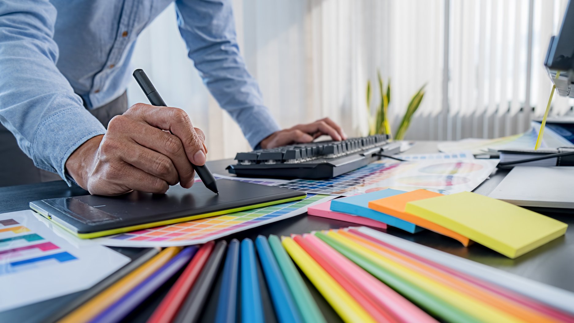 Graphic Designer Draws on Tablet next to Colored Palette 